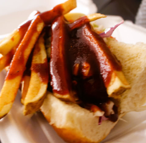 A close up of a polish sausage topped with pulled pork